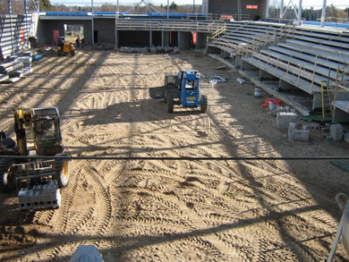 With the tiered, concrete bench seating area already in place, workers use forklifts to move cement blocks across the dirt floor, which will become the arena ice pad