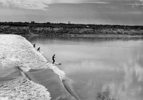 Three surfers ride a wave in a river.