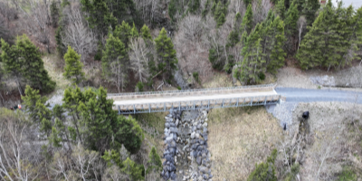 Areal view of a wood and metal pedestrian bridge crossing a wide but shallow culvert