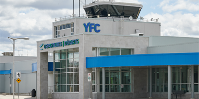 Exterior view of the Fredericton International Airport (YFC) terminal. The letters YFC can be seen on the side of the building. A control tower rests on top.