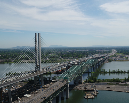 Aerial view of a modern cable-stayed bridge alongside an older truss bridge, spanning a wide river.