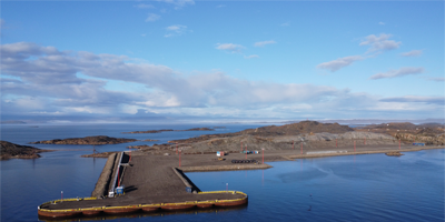A bird's-eye view of a new dock and pier built on gravel, extending into calm blue water with small rocky islands in the background.