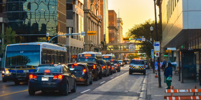 Three transit buses make their way through a busy city street during evening traffic.