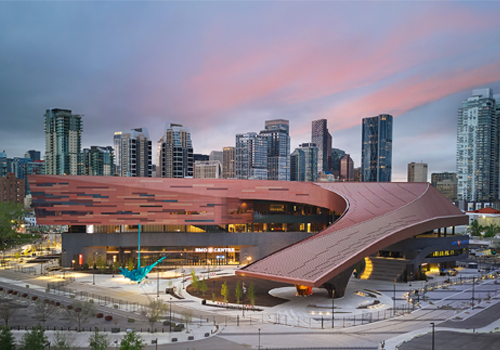 A modern building illuminated under a clear dusk sky, with snow covering the ground around it.