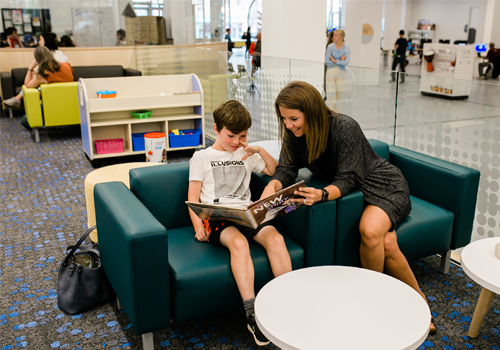 A parent and child sitting together on a couch, looking at a book.