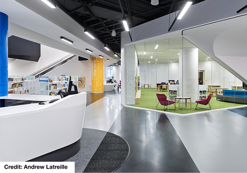 Interior of a children’s library with rows of bookshelves and a table with chairs.