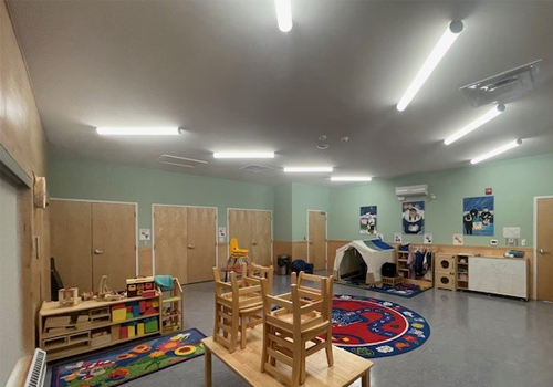 A children’s playroom with colourful rugs, toys, and stacked chairs on a table.