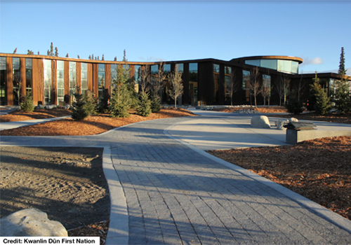 Large wood community building with floor to ceiling windows. Paved walkway and landscaping in front of building.