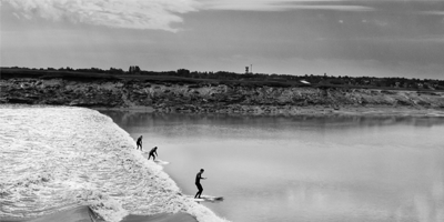 Three surfers ride a wave in a river.