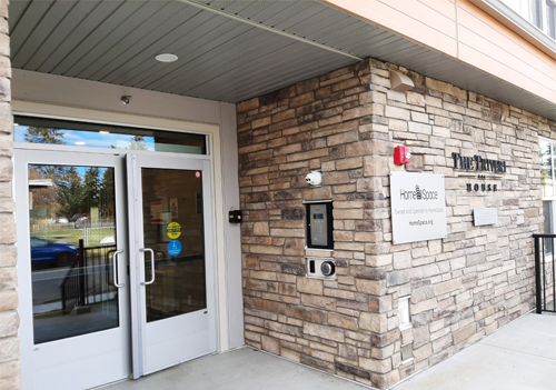 Front entrance of brick building with double doors. ”The Triveri House” on side of building.