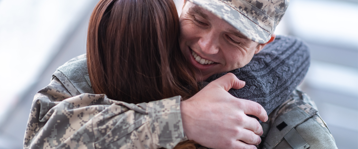 Two people embracing one another. One in Canadian Military Uniform.