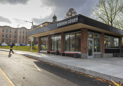 A brick bus station with buildings in the back.