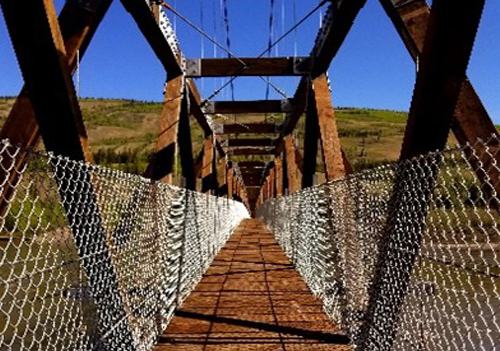 Metal pedestrian suspension bridge from one end. Chain link fence of either side of railings.